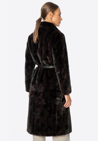 Bruine faux-fur jas met een ceintuur in de taille, lange mouwen en een reverskraag; heeft een zachte, gestructureerde afwerking met subtiele strepen.