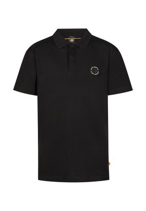 Junge steht, trägt ein schwarzes Poloshirt, blaue Jeansshorts, weiße Socken und weiße Turnschuhe auf hellem einfarbigem Hintergrund.