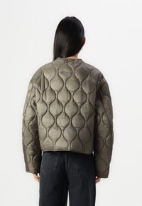 Giacca puffer cropped trapuntata in verde oliva con una texture lucida. Presenta un collo rotondo e grandi motivi a diamante arrotondati.