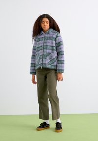 Puffy jacket with purple and green stripes, zipper closure, two side pockets. Paired with olive green pants and black sneakers.