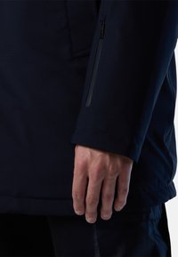 Námořnická voděodolná bunda s texturovaným povrchem, která má zipovou kapsu na rukávu a kontrastní černé zipové detaily.