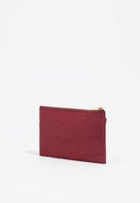 Bolsita de tela burdeos con una superficie texturada, cuenta con una cremallera dorada lisa y tiene una forma rectangular compacta. Adecuada para pequeños objetos.