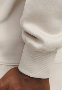 Lichtbeige sweatshirtmanchet gemaakt van zacht materiaal met ribbelstructuur. Heeft een ontspannen pasvorm en zichtbare stikdetails langs de naad.