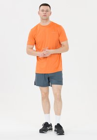 Herrernas träningsoutfit med en ljusorange T-shirt med kort ärm och mörkgrå shorts, samt svarta löparskor och vita strumpor.