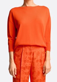 Feloranje gebreide trui met een geribde ronde hals en lange mouwen, gecombineerd met bijpassende oranje broek met een subtiel bloemenpatroon.