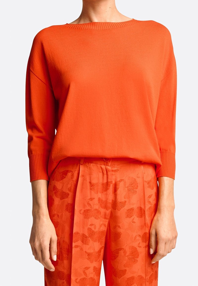 Feloranje gebreide trui met een geribde ronde hals en lange mouwen, gecombineerd met bijpassende oranje broek met een subtiel bloemenpatroon.