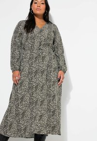 Schwarz-weiß gemustertes Maxikleid mit langen Ärmeln, V-Ausschnitt, tailliertem Schnitt und fließendem Rock. Getragen mit schwarzen Stiefeln und Accessoires.