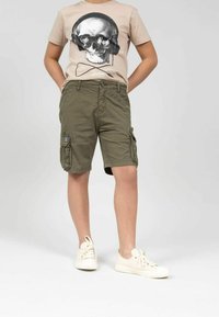 Shorts cargo khaki avec plusieurs poches, dotés d'une fermeture boutons et zip. Associés à un t-shirt graphique beige clair avec un design de crâne.