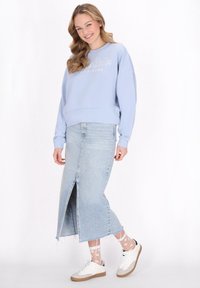 Felpa azzurra chiara con la scritta "Happiness"; abbinata a una gonna di jeans chiara con uno spacco anteriore; sneakers bianche con dettagli grigi.