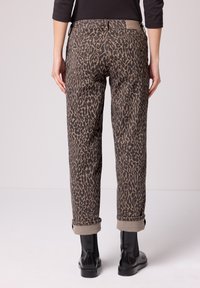 Ruskeat leokuosilliset housut käännetyillä lahkeensuilla, valmistettu pehmeästä kankaasta, joissa on kaksi takataskua ja nimikirjaimilla varustettu vyötärökaitale.