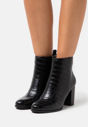 Bottines noires en cuir synthétique texturé avec un motif crocodile, dotées d'un talon bloc et d'une fermeture éclair sur le côté.
