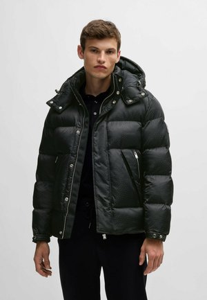 Giacca a vento nera con texture trapuntata, chiusura a zip e bottoni a pressione, cappuccio regolabile e tasche laterali. Fodera interna visibile.