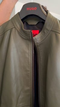 Olive green leather jacket with a round collar, featuring a front zipper and visible stitching detail. The interior is lined in black.