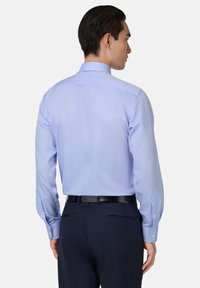 Světle modrá košile s dlouhým rukávem, límečkem, manžetami na knoflíky a hladkou texturou, nošená s tmavými kalhotami a černým pásem.