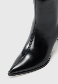 Botte en cuir noire à bout pointu avec couture centrale et finition lisse sur fond blanc.