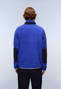 Blue fleece pullover with a high collar, contrasting black elbow patches, and elastic cuffs, featuring a clean, smooth texture.