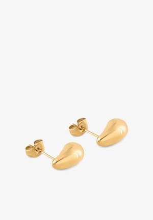 Fiatal fekete nő rövid, göndör hajjal, fekete pántos toppban és apró arany karika fülbevalókkal, jobbra nézve.