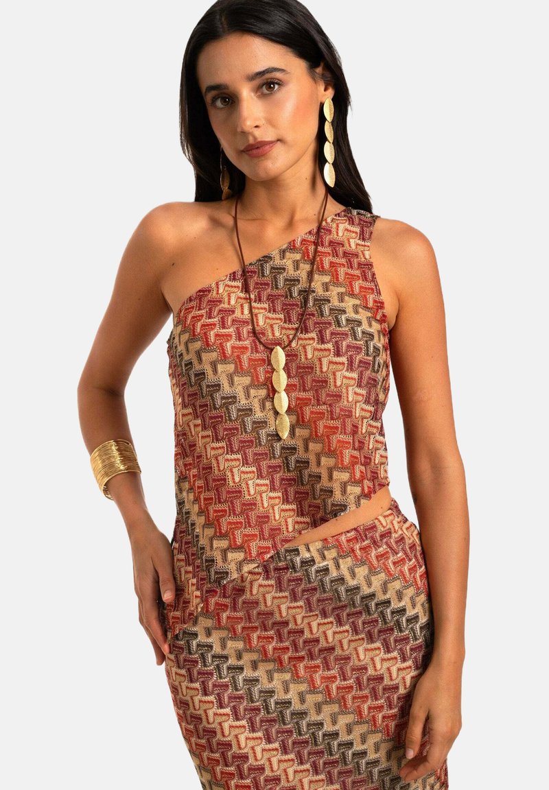 Top tejido asimétrico en tonos cálidos de rojo, marrón y beige, con patrones geométricos. Combinado con una falda de patrón a juego.