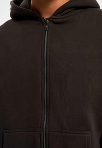 Felpa nera con zip realizzata in tessuto morbido. Caratterizzata da una cerniera frontale e due tasche frontali. Texture liscia con cappuccio.