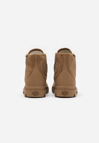 Bottines en toile marron avec une semelle en caoutchouc, présentant un logo rond de chaque côté et une languette à l'arrière pour un enfilage facile.