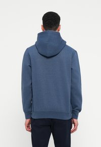 Μπλε φούτερ με κουκούλα, κατασκευασμένο από υφασμάτινη υφή. Διαθέτει ραμμένα μανίκια και στρίφωμα. Απλό σχέδιο, χωρίς ορατά λογότυπα ή σημάδια.