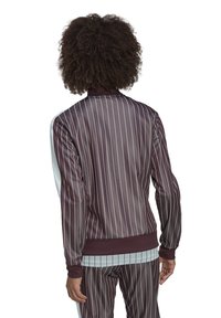 Bordeauxfarbene Polyesterjacke mit weißen vertikalen Streifen, gerippten Ärmelbündchen und hohem Kragen. Glatte Textur, taillierte Passform und sichtbare passende Hose.