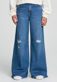 Jeans in denim blu a gamba larga con strappi e usura. Presentano un'alta vita, orlo sfilacciato e il classico design a cinque tasche.