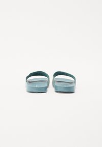 Türkise Rutsch-Sandalen mit glatter, glänzender Oberfläche, minimalistischen Design, offener Rückseite und breiten Riemen. Strukturiertes Fußbett für zusätzlichen Komfort.