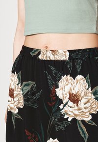 Falda negra con grandes flores beige y hojas verdes. Cintura elástica y textura suave, con un diseño fluido que se drapea cómodamente.