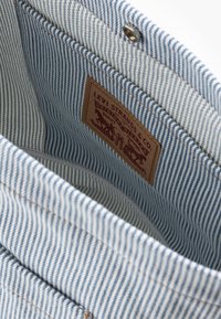 Modrý a bílý pruhovaný textilní vnitřek tašky s koženou nášivkou s logem "Levi Strauss & Co." a kovovým zacvakáváním.
