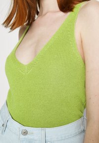 Grön stickad linne med V-ringning, med texturerad ribbning. Tillsammans med ljusblå högmidjade denimshorts.