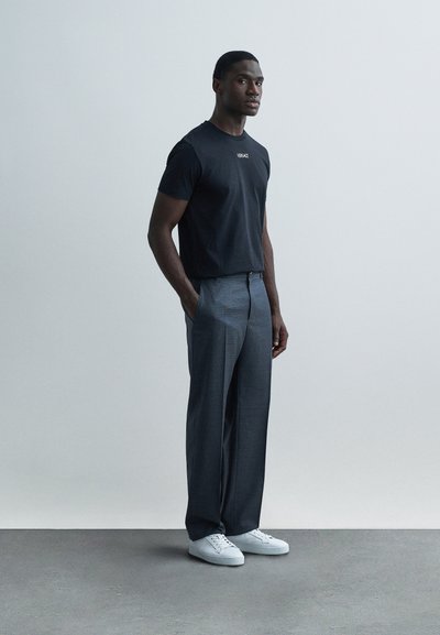 Μαύρο κοντομάνικο μπλουζάκι με λογότυπο, γκρι παντελόνι σε ίσια γραμμή και λευκά αθλητικά παπούτσια. Λείο ύφασμα, σχέδιο με ευθεία φόρμα, μινιμαλιστικό στιλ.