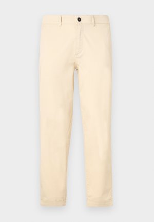 Beige chinos made of smooth cotton fabric, featuring a zip fly, button closure, and rolled cuffs. Straight-leg design with minimal detailing.