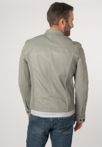 Lichtgrijze leren jas met een getailleerd ontwerp, voorzien van gestikte accenten, een gestructureerde rug en drukknoopsluitingen op de manchetten. Denim jeans zichtbaar.