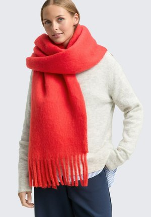 Écharpe en laine rouge vif avec une texture douce, présentant des franges aux extrémités. Portée lâchement autour du cou par-dessus un pull léger.