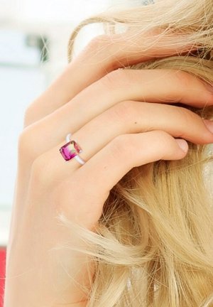 Zilveren ring met een vierkante, roze edelsteen in een klauwzetting, met een gladde band en twee kleine accentstenen.