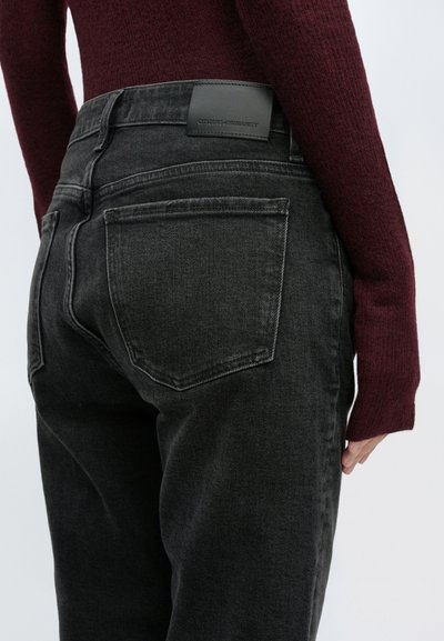 Čierne rifle z denimu majú vysoký pás, priamy strih nohavíc a zadné vrecká. Na pásiku je viditeľná kožená značka značky.