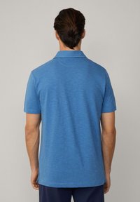 Modro krátký rukáv polo tričko s měkkou strukturou, klasickým límečkem a bočními rozparky na spodním okraji. Zadní pohled ukazuje hladkou tkaninu a švy.