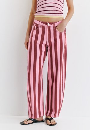Persoană purtând pantaloni largi cu talie înaltă cu dungi verticale roz și maro, un crop top roz cu dungi și papuci negri.