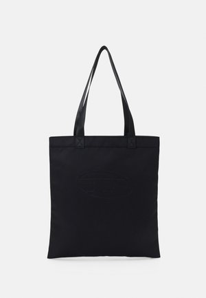 Sort mulepose med to lange håndtag og et diskret præget logo, vist oprejst mod en ensartet, lys grå baggrund.