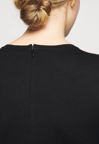 Haut noir à côtes avec encolure ronde et fermeture éclair visible dans le dos. Texture lisse et design ajusté.