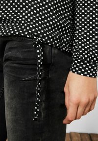 Top a maniche lunghe con motivo bianco e nero, dotato di un cordino in fondo, abbinato a pantaloni in denim neri. Tessuto liscio.