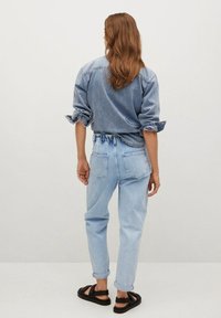 Chemise en denim bleu clair à manches roulées, associée à un jean bleu clair avec taille à cordon, et des sandales noires.