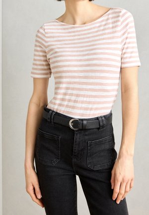 Frau trägt ein hellrosa-weiß gestreiftes Kurzarmoberteil, das in eine hochtaillierte schwarze Jeans mit schwarzem Gürtel gesteckt ist.