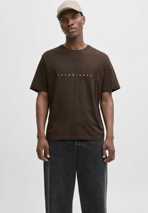 Brown cotton t-shirt featuring short sleeves and a crew neck, with "JACK&JONES" printed in white across the chest. Worn with black jeans.