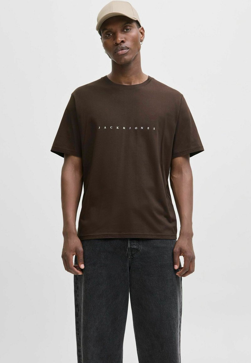 Brun bomulds t-shirt med korte ærmer og rund hals, med "JACK&JONES" trykt i hvid på brystet. Båret med sorte jeans.