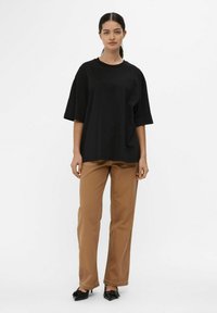 Black oversized T-shirt with short sleeves and crew neck. Paired with light brown straight-leg pants and black bow-detail flats.