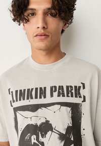 Maglietta grigia in cotone con una grande stampa grafica bianco e nero dei Linkin Park. Design classico con scollo a girocollo e maniche corte.