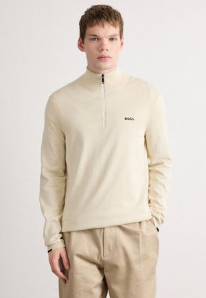 Lichtbeige zip-up vest van zacht materiaal met een hoge kraag en ribgebreide accenten, voorzien van een klein zwart "BOSS" logo op de borst.