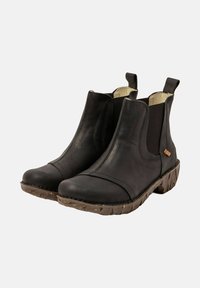 Botas de tobillo de cuero negro con paneles laterales elásticos, lengüetas para tirar y suelas de goma marrón texturizadas, mostradas sobre un fondo blanco.